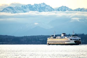 A large white boat is sailing on the water in front of a snowy mountain range.
